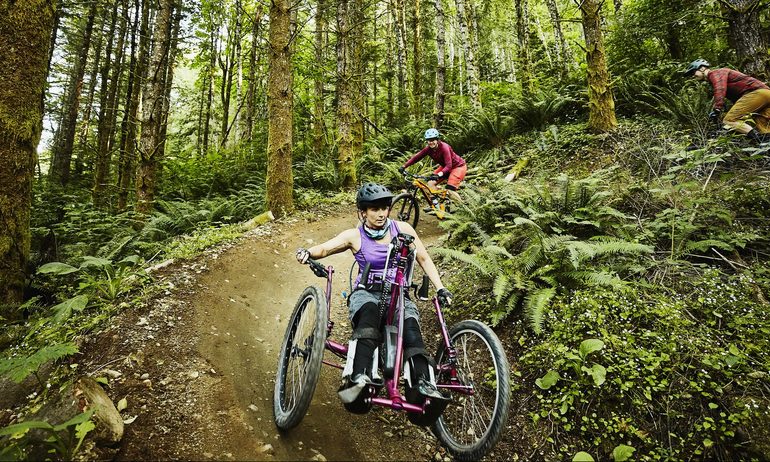 Female wheelchair athlete riding mountain bike on trail with friend