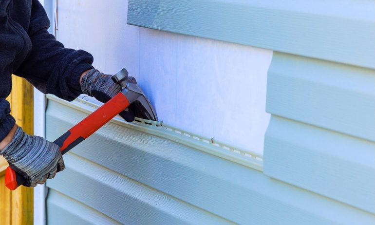 Worker replacing vinyl siding on house