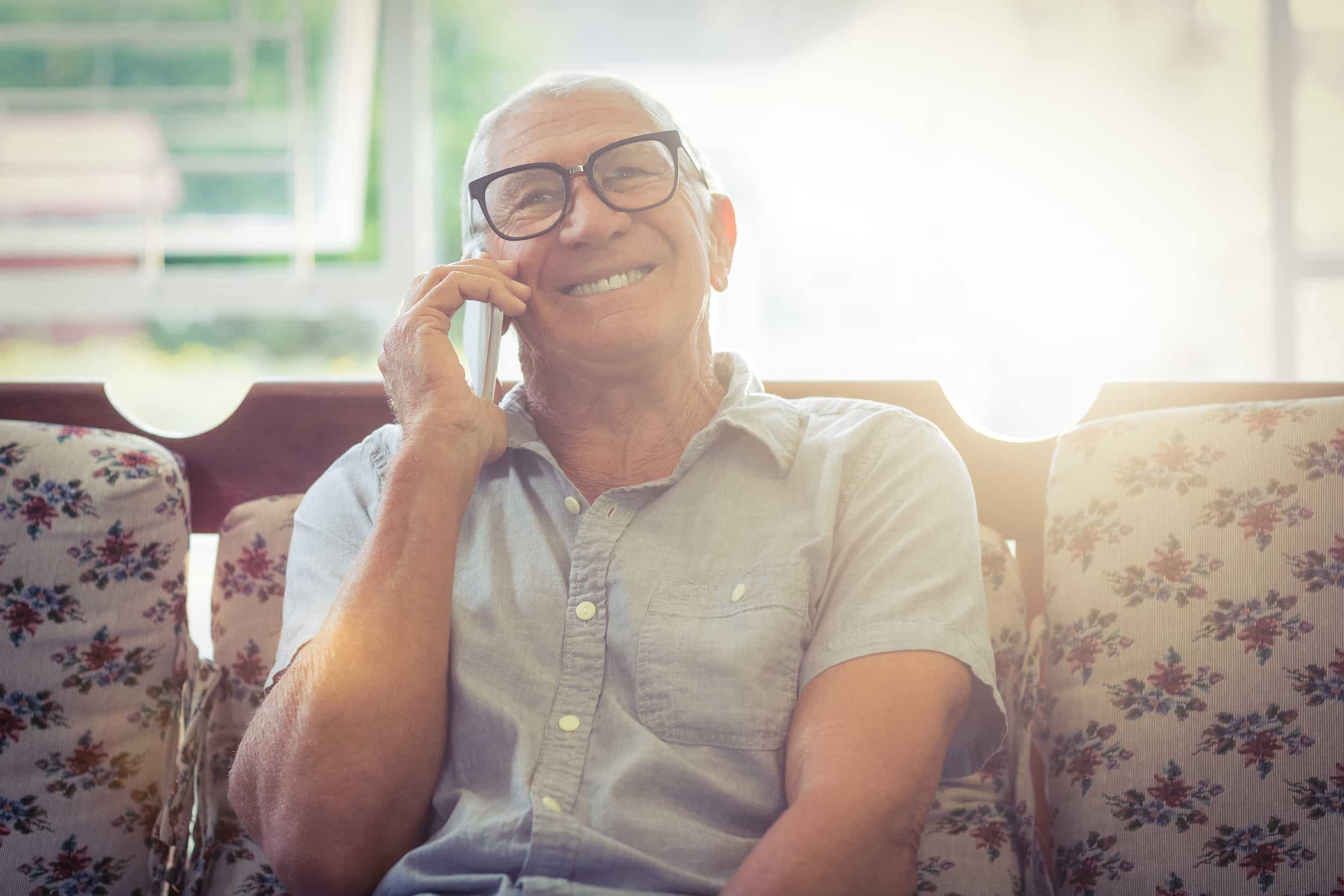 Gentlemen sitting on couch, on a cell phone, receiving counseling from Money Fit about his reverse mortgage options.