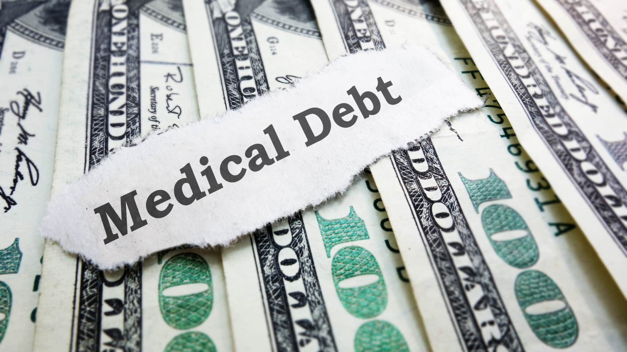 The words medical debt on top of 100 dollar bills.