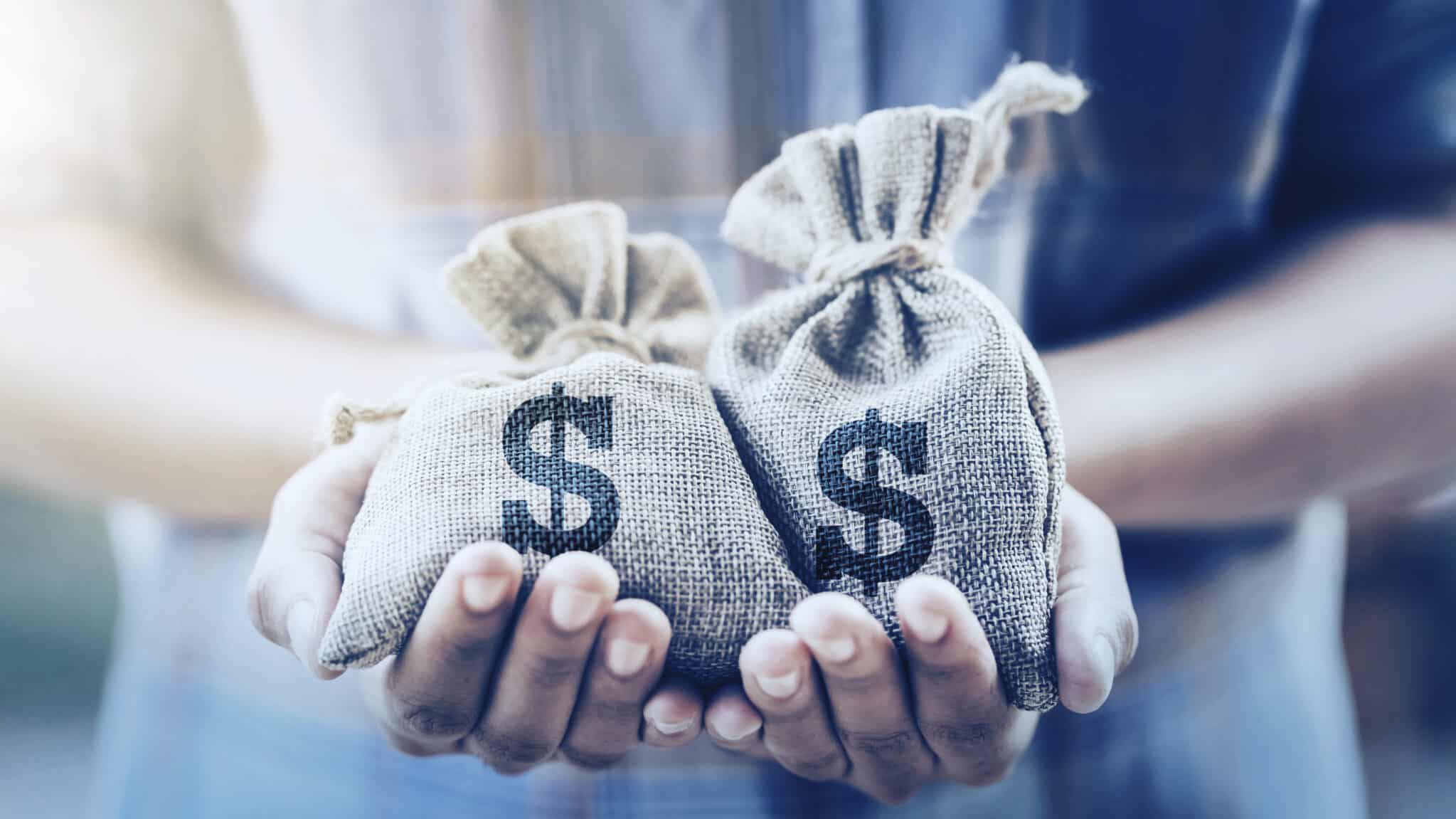 hand holding two money bags showing paying debt vs saving money