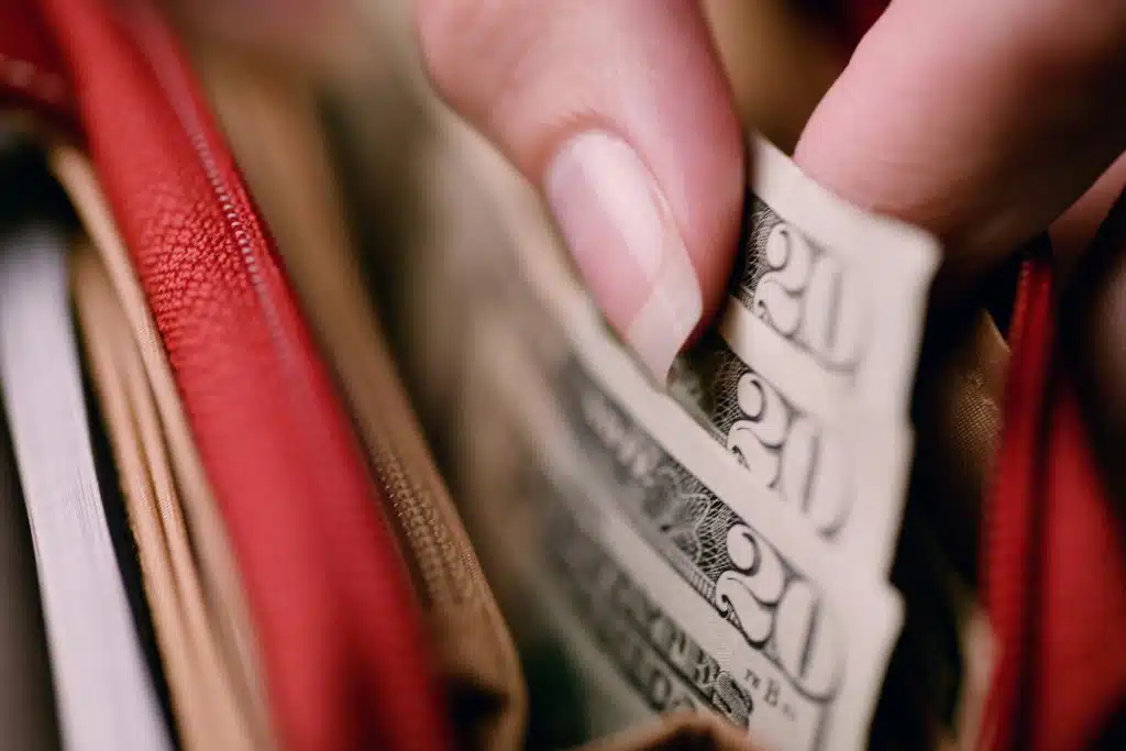 Picture of a hand grabbing 20 dollar bills in a red purse